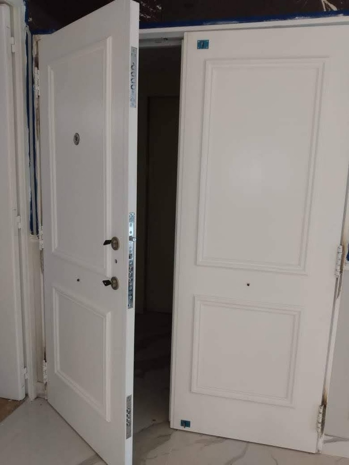 Puerta acorazada doble blanca abierta mostrando el sistema de cierre multianclaje en el canto