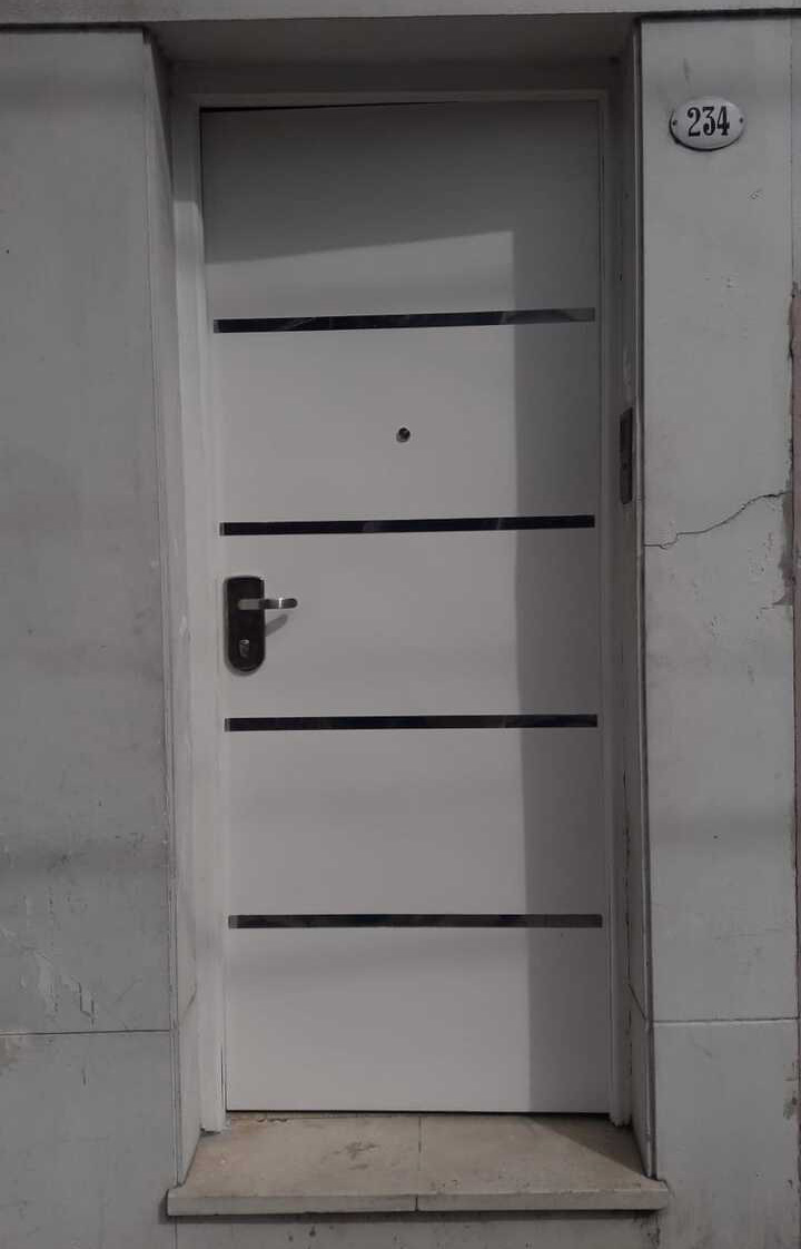 Puerta blindada blanca con detalles metálicos horizontales instalada en frente de vivienda