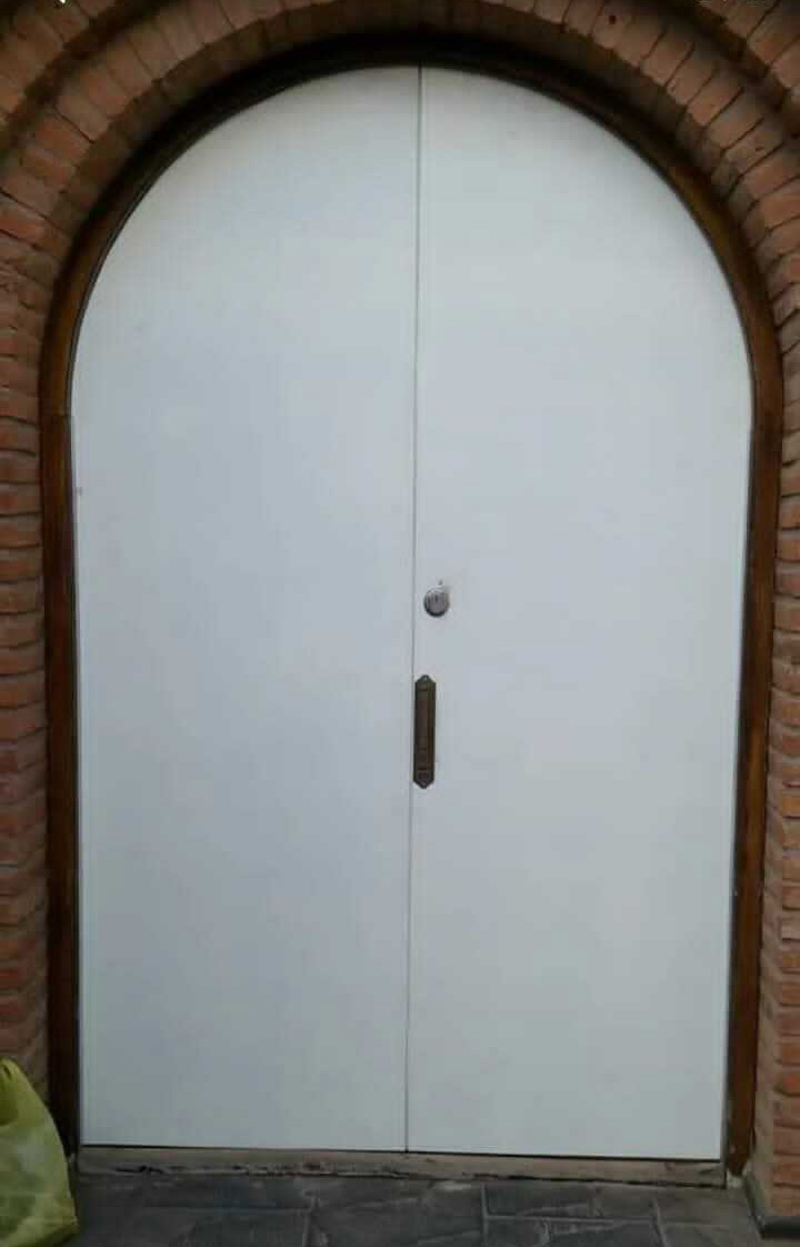 Puerta blindada de exterior blanca con forma de arco y marco de ladrillo visto, instalada en entrada principal