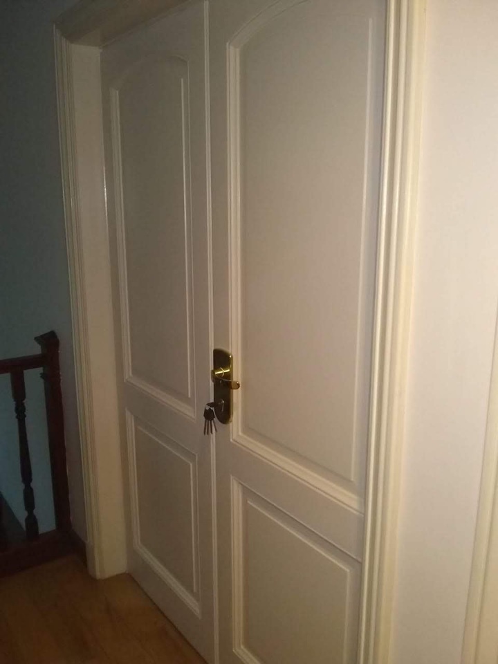 Puerta blindada doble de interior color crema con paneles decorativos, picaporte dorado y llave puesta