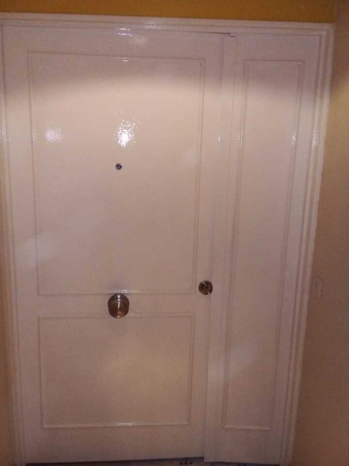 Puerta blindada interior blanca con molduras clásicas y pomo central plateado