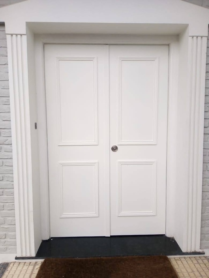 Puerta de seguridad doble blanca con molduras instalada en entrada principal exterior